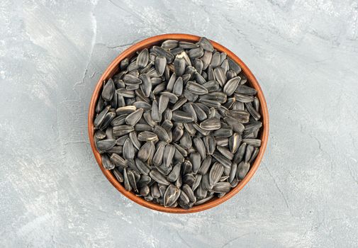 Large ceramic bowl with sunflower seeds on concrete background, top view