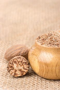 Spice nutmeg in the wooden jar on the burlap closeup