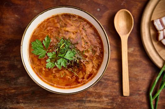 Flat lay of national Ukrainian dish - Borscht - served in a bowl with parsley and dill on a wooden table. Traditional Ukrainian and Russian cuisine, beet soup borscht. Copy space for advertising text