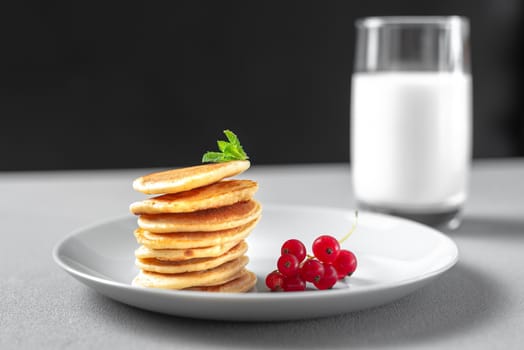 Mini pancakes with blueberries and raspberries. American breakfast on a dark background. Healthy eating for the whole family. Homemade pancakes with berries. A glass of milk in the background. Breakfast for the whole family on the black and white background