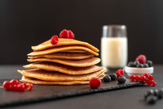 Mini pancakes with blueberries and raspberries. American breakfast on a dark background. Healthy eating for the whole family. Homemade pancakes with berries.