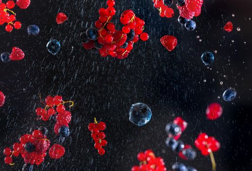 Fresh berries on a black blue background with water droplets flying in different directions. Many different berries in the form of a frame on a dark background. The concept of veganism and vegetarianism. Vegan diet fleckitarians diet