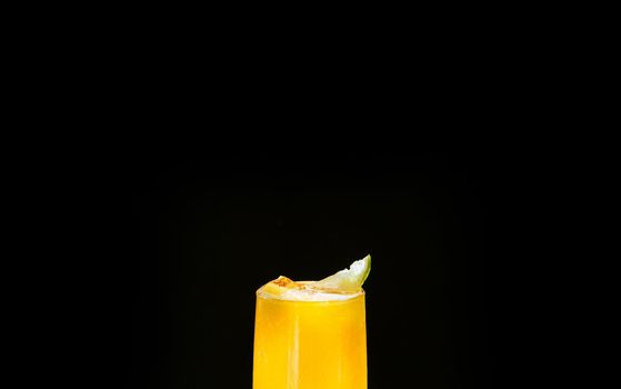 A Mexican smoothie drink made from mango, chili peppers, salt, and lime. A refreshing summer smoothie on a black background of bright orange