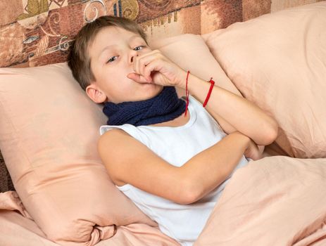 Portrait of a sick young boy coughing in bed