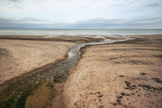 Empty beach, with water stream leading to sea, on overcast day. Portobello, Edinburgh