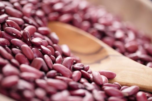 Close up of dried red beans at an angle with wooden spoon and shallow depth of field.