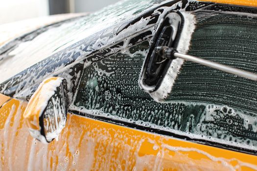 Side window of yellow car washed in self service carwash, brush leaving strokes on glass covered with shampoo foam.