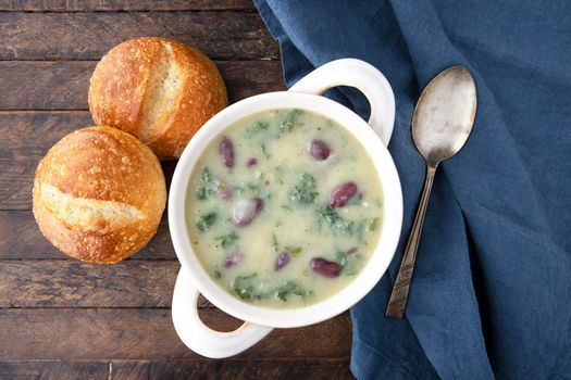 Portuguese Caldo Verde soup flat lay with bread, napikin and spoon on dark wooden table.