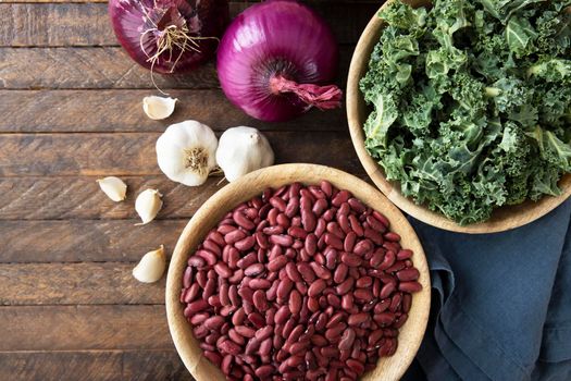 Flat lay on dark wooden table with dried beans, kale, onion and garlic.