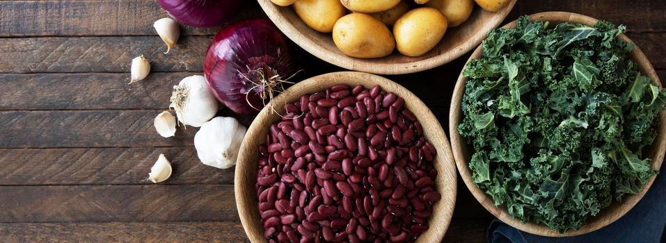 Flat lay on dark wooden table with dried beans, kale, onion and garlic. Sized for use as banner.