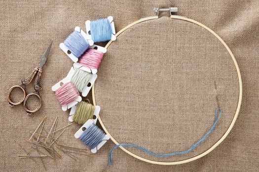 Embroidery floss, vintage style scissors, wooden hoop and needles with cotton linen cloth in hoop, flat lay with copy space