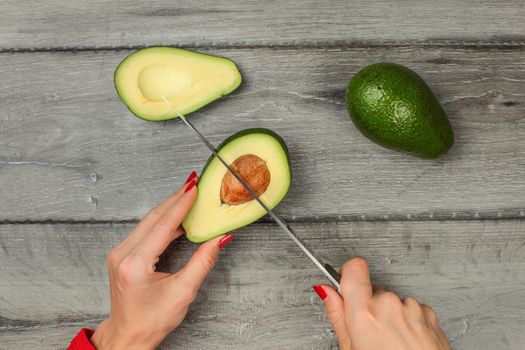 Tabletop view - woman hand holding chef knife, removing seed from avocado cut in half.