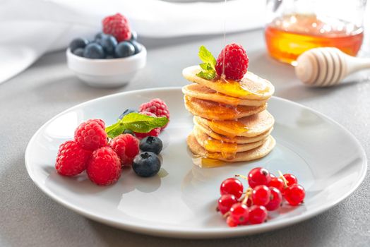 Mini pancakes with honey and berries. An American traditional breakfast. Breakfast for the whole family. Healthy Eating. Honey poured over the pancakes. Food for breakfast healthy eating. Pancakes without butter with berries. Food for vegetarians and for dieting. American Pancakes Mini.