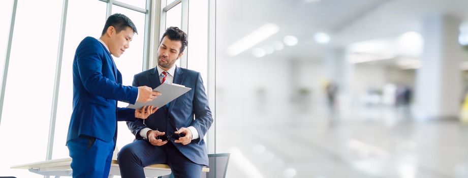 Two business people talk project strategy at office in widen view meeting room. Businessman discuss project planning with colleague at modern workplace .