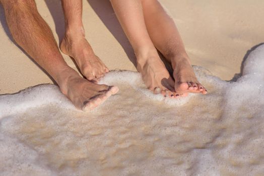 Two pairs of legs on white sand with a wave