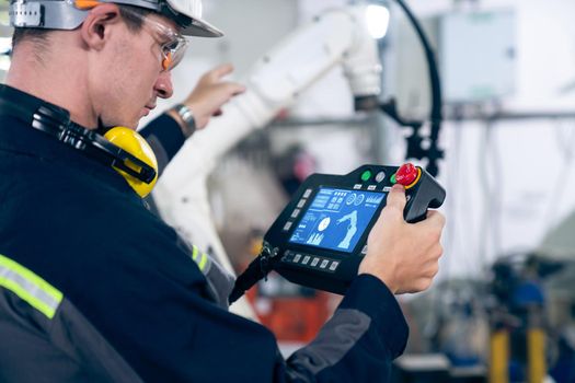 Young factory worker working with adept robotic arm in a workshop . Industry robot programming software for automated manufacturing technology .