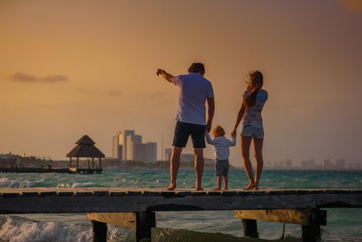 Family on the beach at sunset standing on the pier. Wooden walkway.