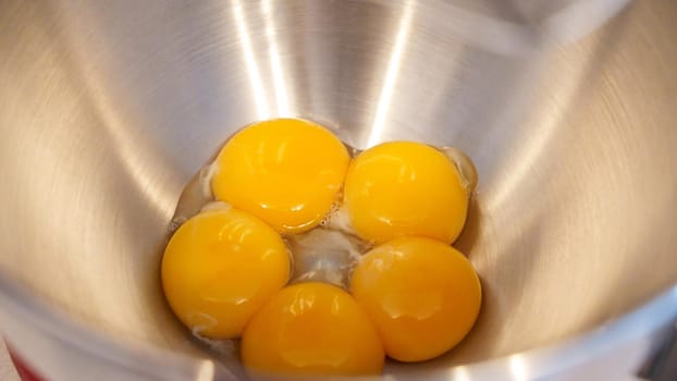Raw eggs in a metal bowl of standing mixer. Preparing egg yolk with sugar in kitchen mixer