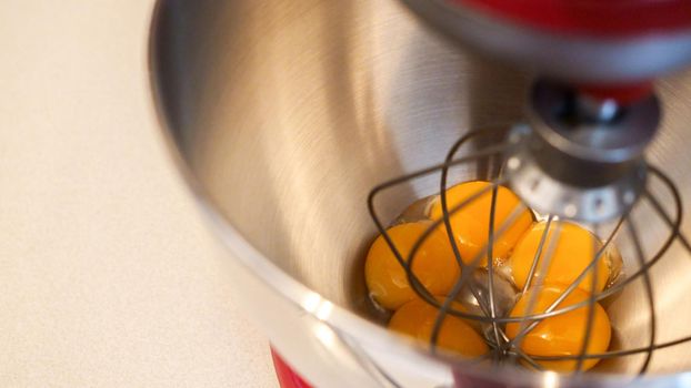 Close up view yellow eggs in a metal mixer bowl. Red stand mixer with white background.