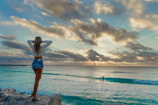 Slender blonde woman admires the sunrise at sea.