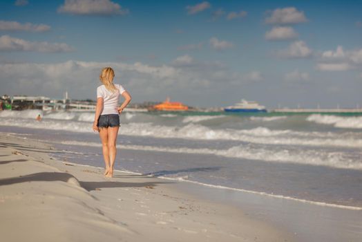 Slender blonde woman admires the sunrise at sea.