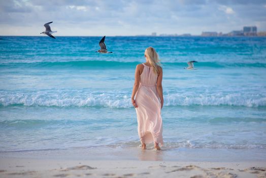 Slender blonde woman admires the sunrise at sea.