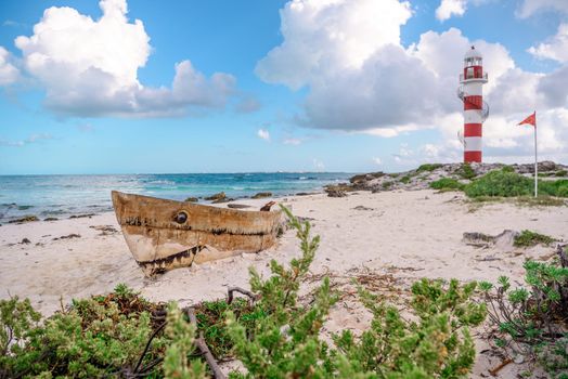 Old boat on the beach and lighthouse in Cancun.