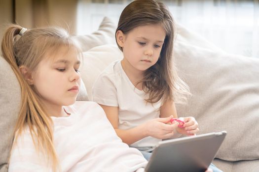 Two little sisters Lying On Couch And Using Tablet