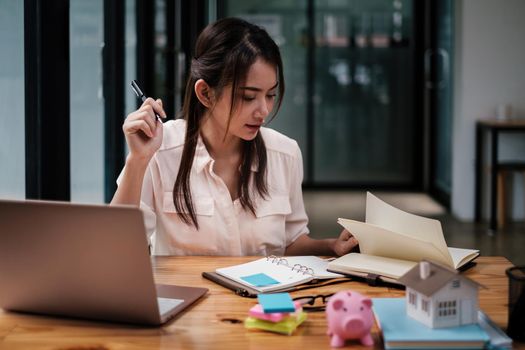 Architect woman hand-draw a design house with a model on a wooden desk. Property idea in real estate