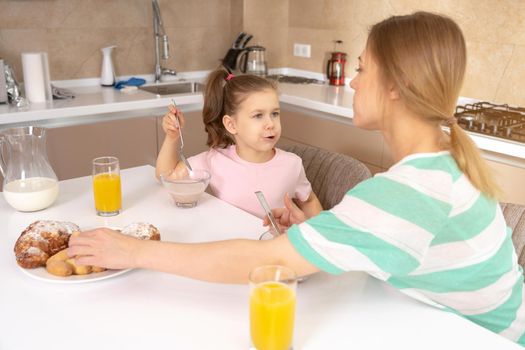 Mother serving breakfast to her two daughters at a table in kitchen