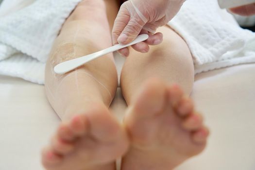 Cosmetologist preparing female patient for laser hair removal on legs