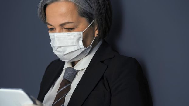 Mature masked business woman using digital tablet. Close up shot.