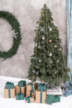 New Year's tree is decorated with garlands and balloons, under the tree are gifts with bows. Christmas wreath in the background. High quality photo.