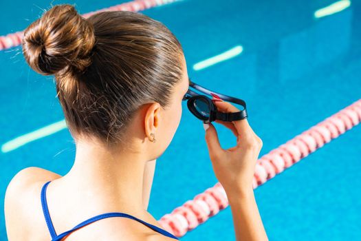 Young woman in swimming pool holding goggles