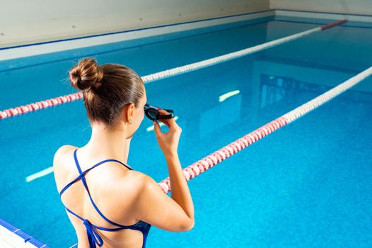 Young woman in swimming pool holding goggles