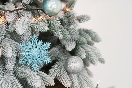 Artificial Christmas Tree close-up. Light branches are decorated with balloons and garland. On a branch hangs a blue snowflake. High quality photo.
