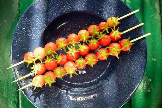 Photographic representation of three skewers made with red and tasty cherry tomatoes from Pachino, Sicily Italy placed over blue plate. 