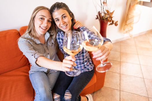 Two happy lesbian girls toasting with champagne on sofa looking at camera celebrating freedom of choice and living together in new modern family concept against sexism and social differences