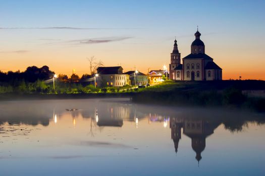 The night town is reflected in the lake. Beautiful sunset and fog over the lake. Peace and tranquility