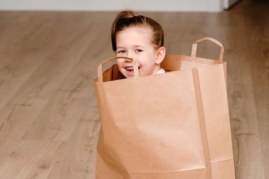 Little girl sitting in Brown paper shopping bag