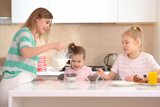 Mother serving breakfast to her two daughters at a table in kitchen