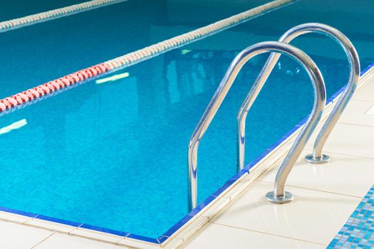 Empty indoor swimming pool with railing and steps