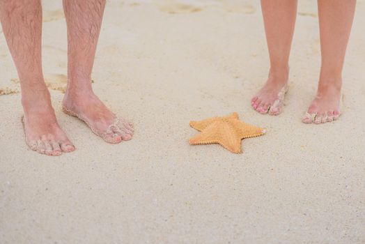 Two pairs of legs on white sand with a wave.