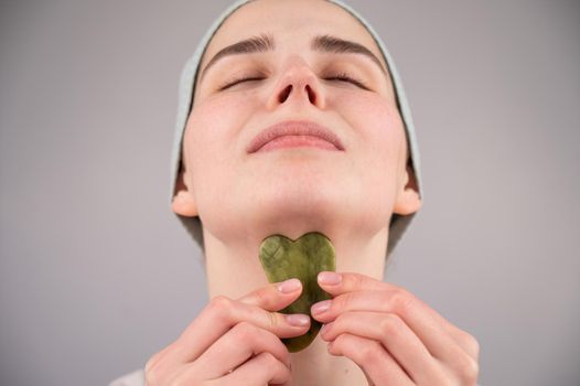 Close-up portrait of a young woman massaging her face with a gouache scraper