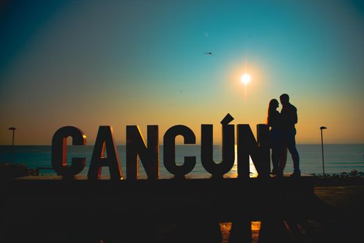 The silhouette of a man and a woman near the inscription Cancun in the background of the sea.