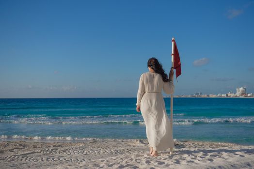 A woman stands on the beach near the red flag. Mexico.