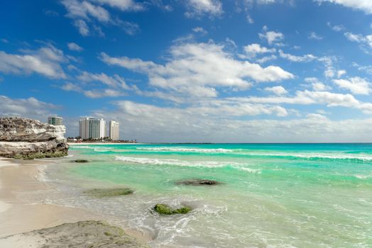 View of sandy beach panorama at bay of Caribbean Sea in mexican city, white hotels buildings and jet skis, clear water and blue sky in warm sunny winter day