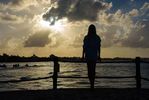 Slender blonde woman admires the sunrise at sea.