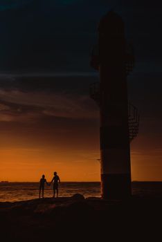 The silhouette of a couple and a huge lighthouse against the backdrop of the sea and the setting sun. Mexico.