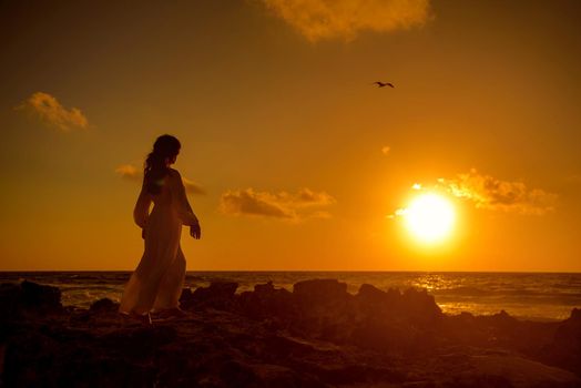 Slender blonde woman admires the sunrise at sea.